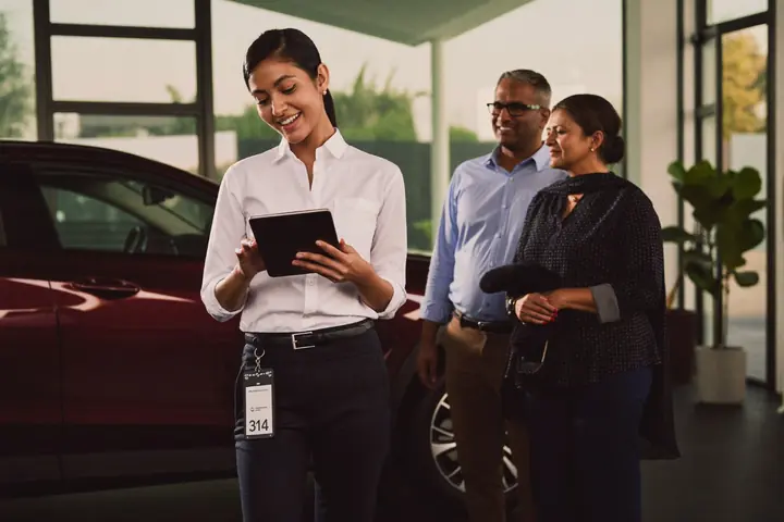 Sales consultant showing a couple car details on a tablet in a showroom